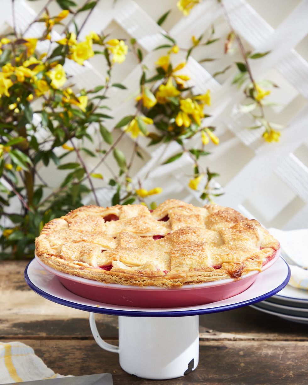 a fruit pie in a pink pie plate perched on a dessert stand made from a vintage enemalware mug and plate