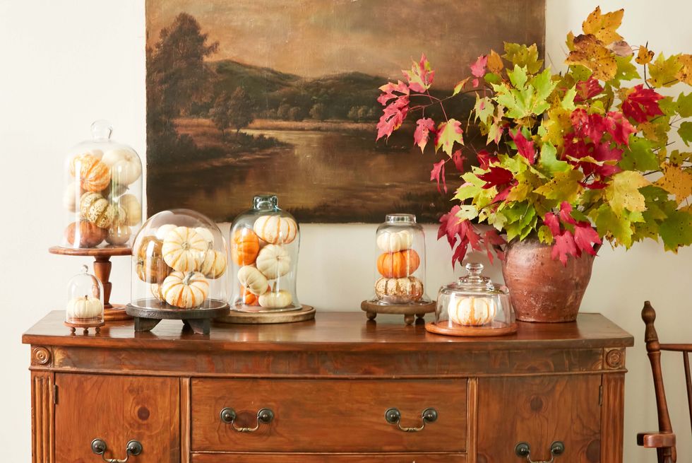 pumpkins nestled in glass clouches on a wood sideboard as diy halloween decorations