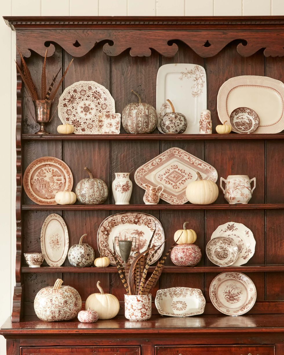 pumpkins made to look like transferware placed among ceramic transferware in wood cabinet as diy halloween decorations