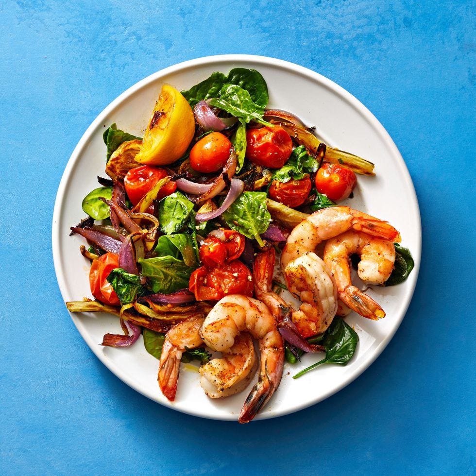 roasted shrimp with a side of tomatoes and spinach served on a plate