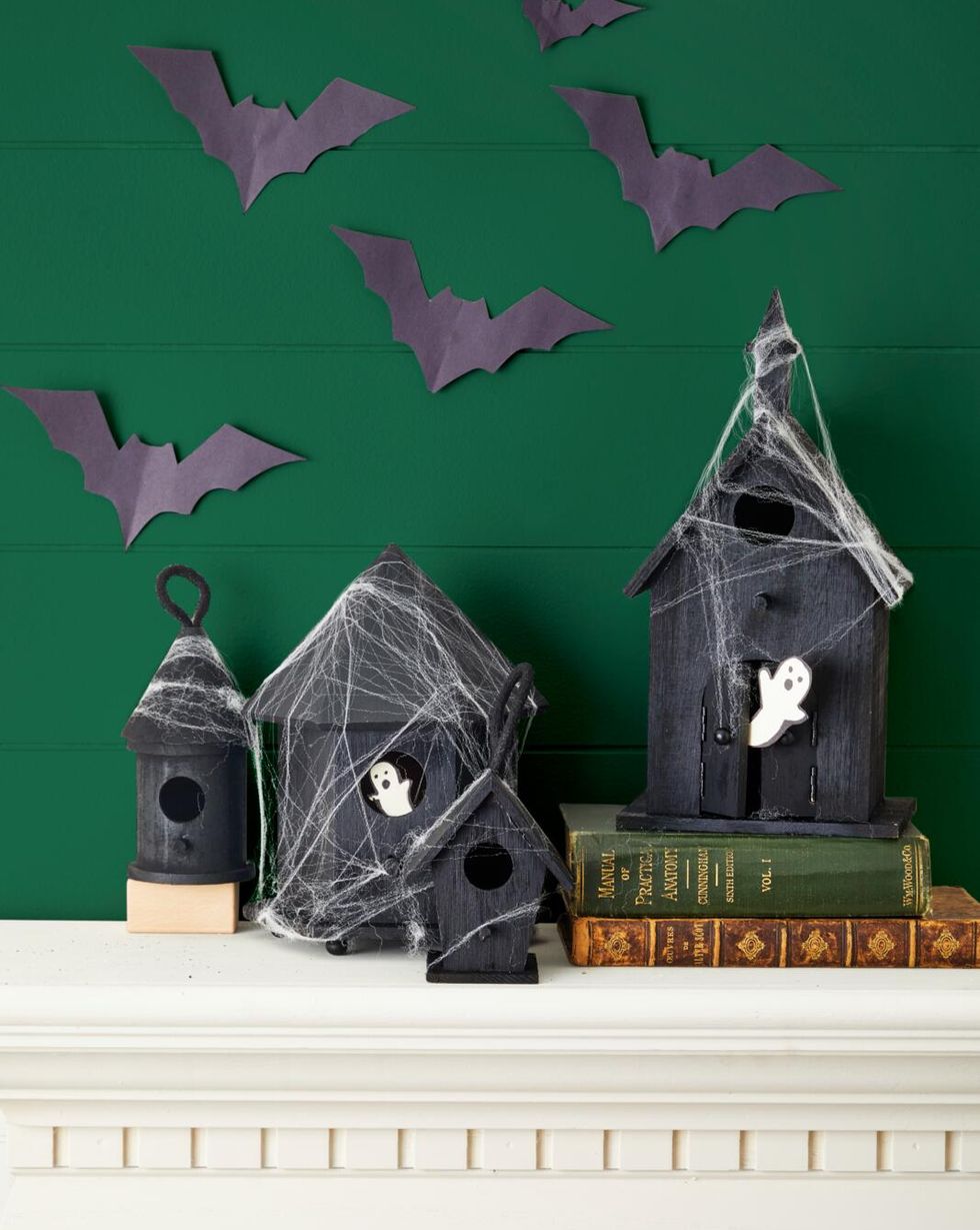 bird houses painted black for halloween set on a mantel draped with fake spider webs