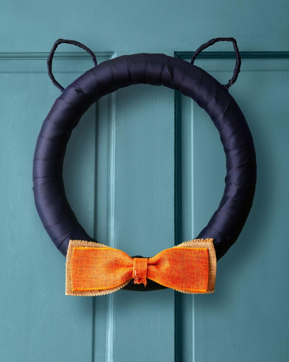 cat wreath with black wire ears and orange bow hung on a blue door