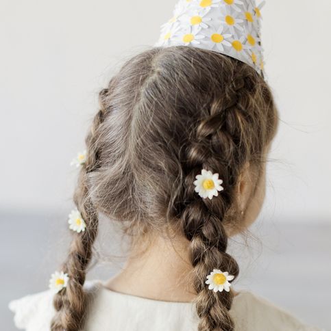 girl with brunette braided hair with white flowers and birthday cone hat with decorative chamomiles on a white wall background