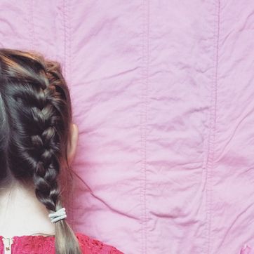 view of the back of a little girls head with french braids and a bright pink dress in front of a pink background
