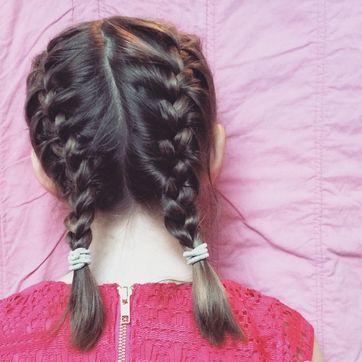 view of the back of a little girls head with french braids and a bright pink dress in front of a pink background