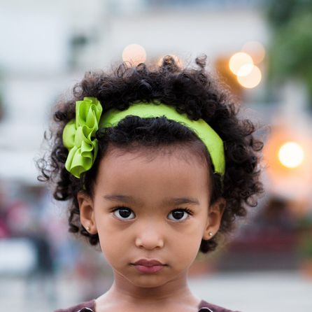 فتاة صغيرة ذات شعر بني مجعد وعصابة رأس خضراء زاهية مع فيونكة