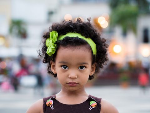 little girl with curly brown hair and a bright green headband with a bow