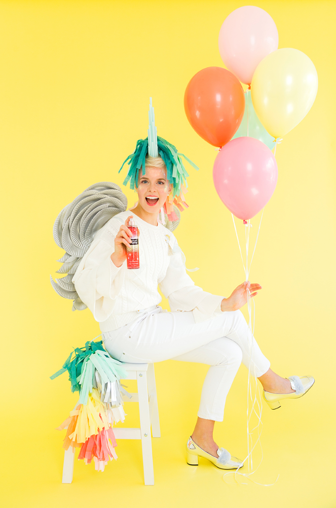 easy halloween costume, woman sitting down on a chair wearing all white and a diy unicorn head and tail with balloons