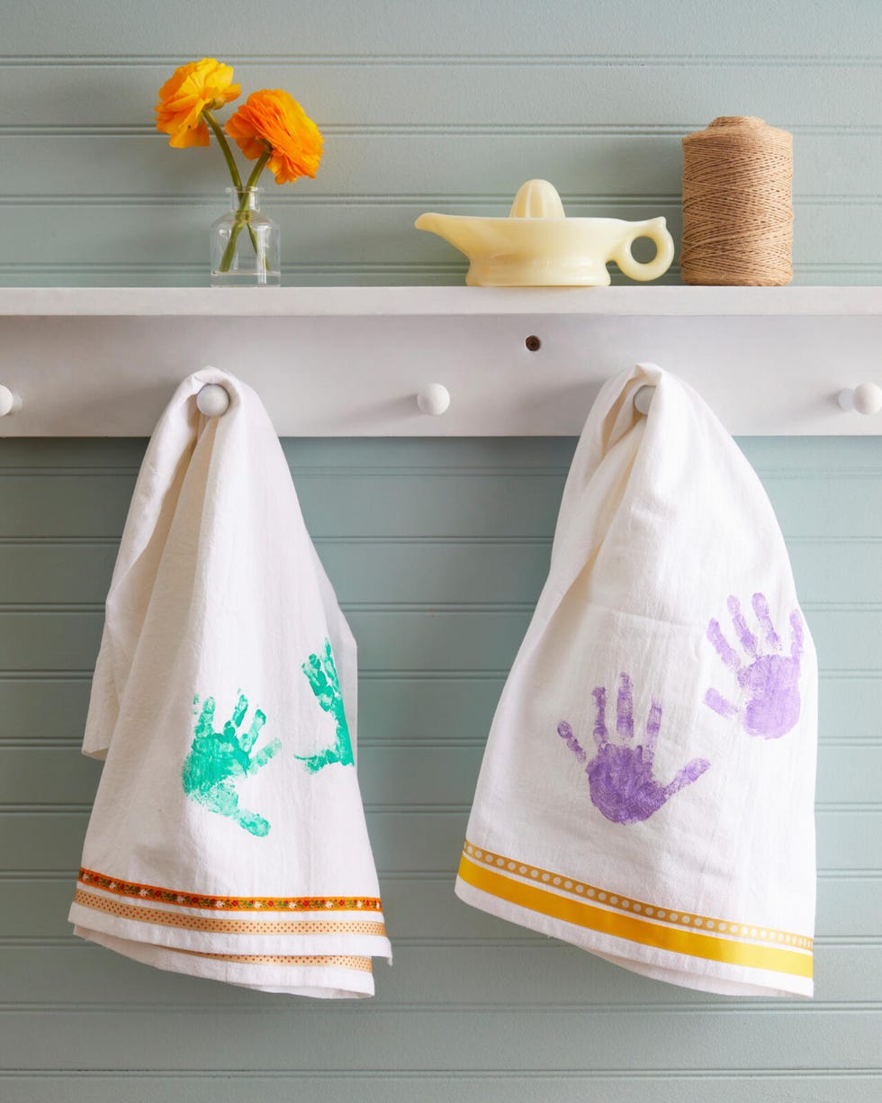 white dishtowels with ribbon sewn on the bottom and kids pain handprints in the middle hung from a shaker peg rail on a light blue background