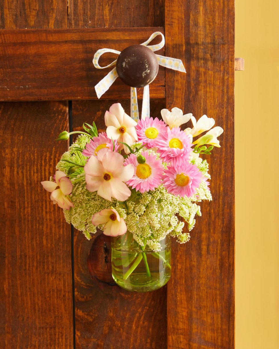 A bouquet of flowers arranged in a vintage green mason jar hanging from a ribbon on a brown door