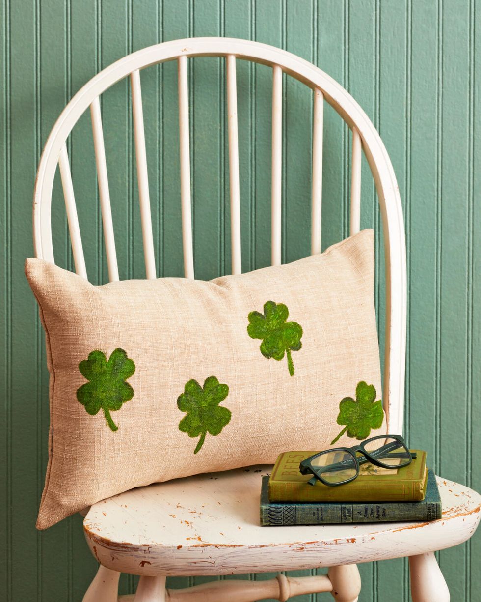 a linen colored pillow with flour leaf clovers painted on it set on a white chair