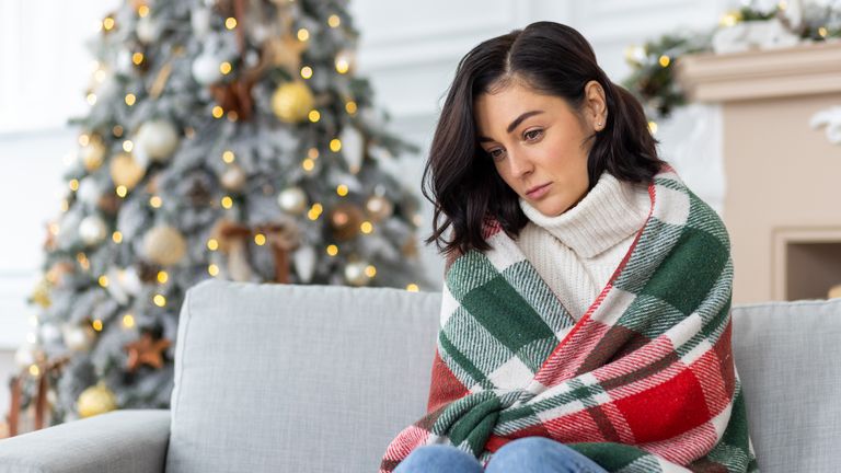 a woman looking sad on a sofa with a christmas tree in the background