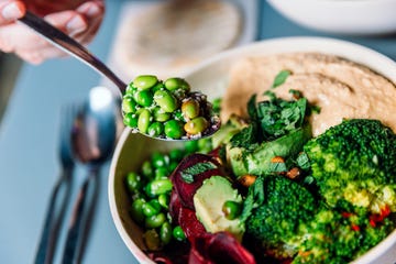 eating vegan bowl with edamame beans, broccoli, avocado, beetroot, hummus and nuts