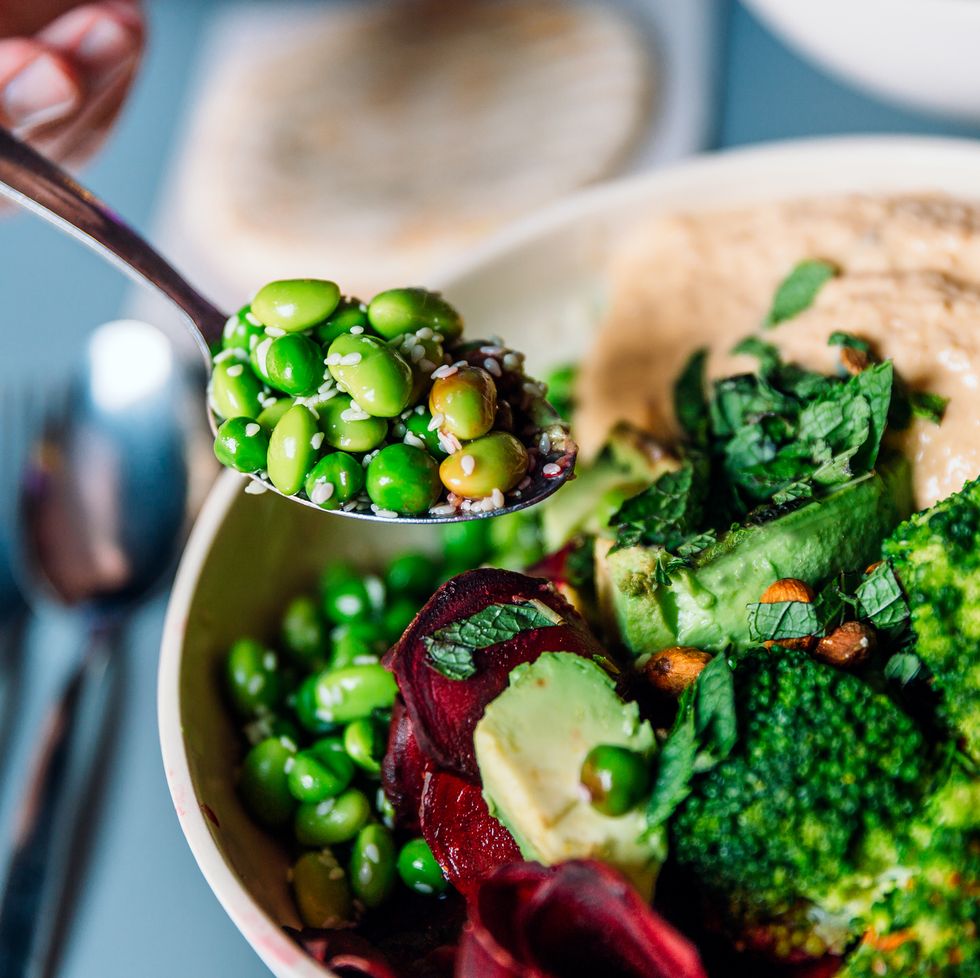 eating vegan bowl with edamame beans, broccoli, avocado, beetroot, hummus and nuts