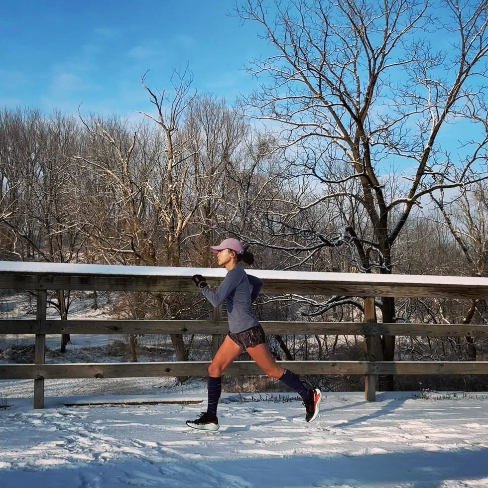 woman jogging on a snowy path near a wooden fence