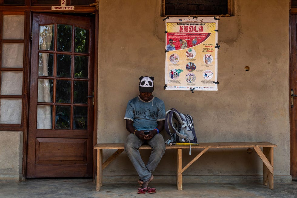 Een jongeman wacht naast de ingang van een privkliniek in Beni Op de muur achter hem hangt een voorlichtingsposter over het voorkomen van ebola