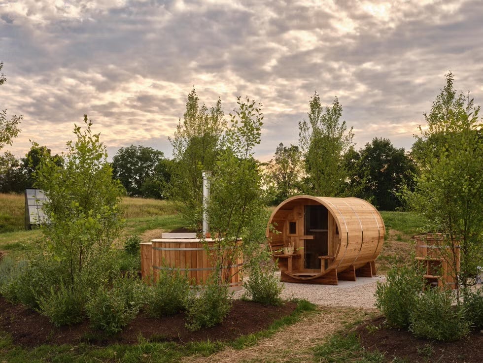 A wooden sauna and hot tub setup surrounded by greenery.