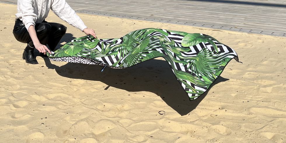 a good housekeeping analyst evaluating a greena nd white eccosophy beach towel on a beach, good housekeeping's best beach towels