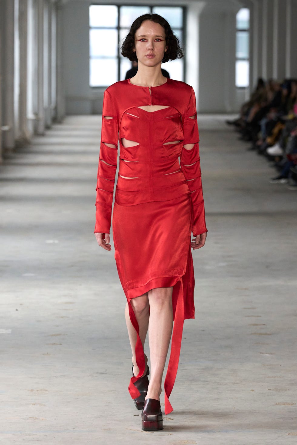 Model showcasing a red cutout fashion dress in a runway setting