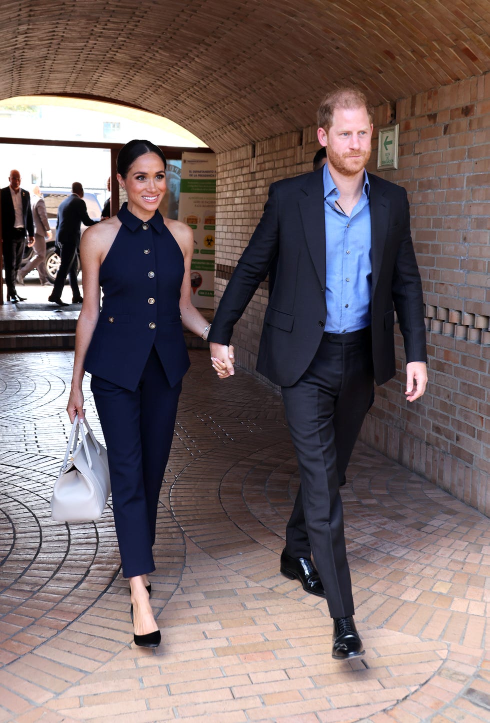 Meghan and Harry walk hand in hand along a cobbled path