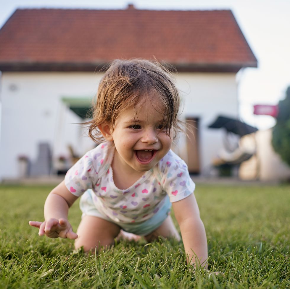 ecstatic baby girl crawling on grass outdoors in a back yard in summer