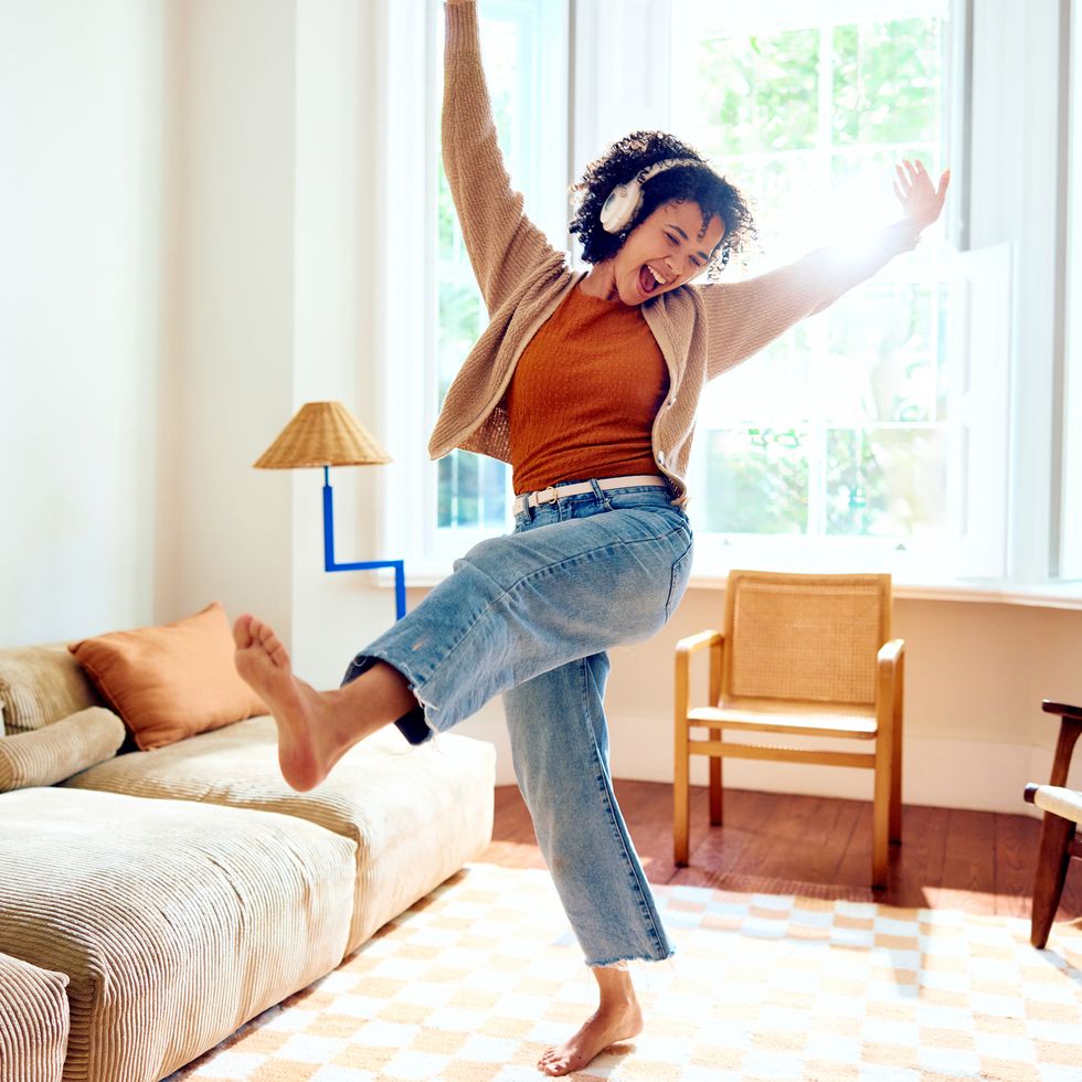 ecstatic young woman wearing headphones, listening to music and dancing barefoot