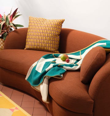 brown sofa with patterned yellow cushion printed throw and plate of fruit