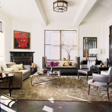 elegant living room with dark floors and black marble fireplace with red face artwork above it and seating areas