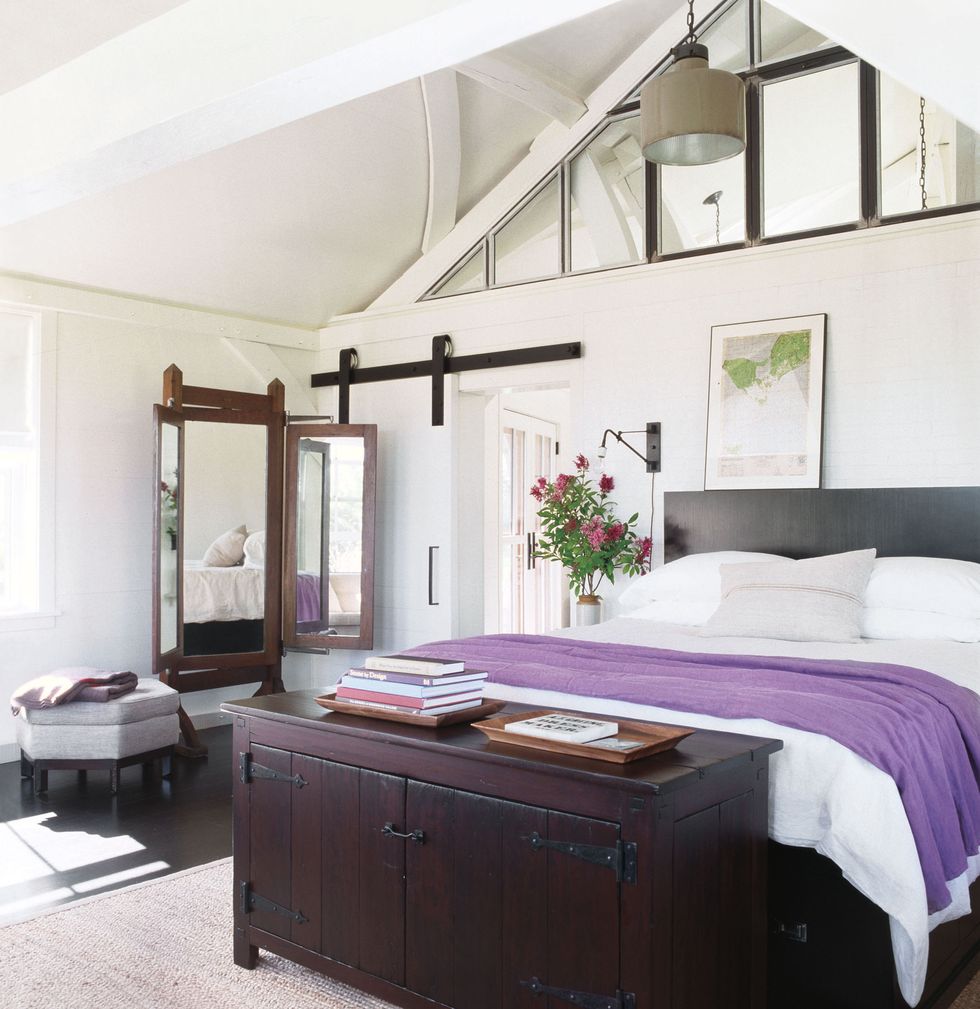 white bedrooms with peaked ceilings and a bed with purple cover and a dark heavy chest at the foot