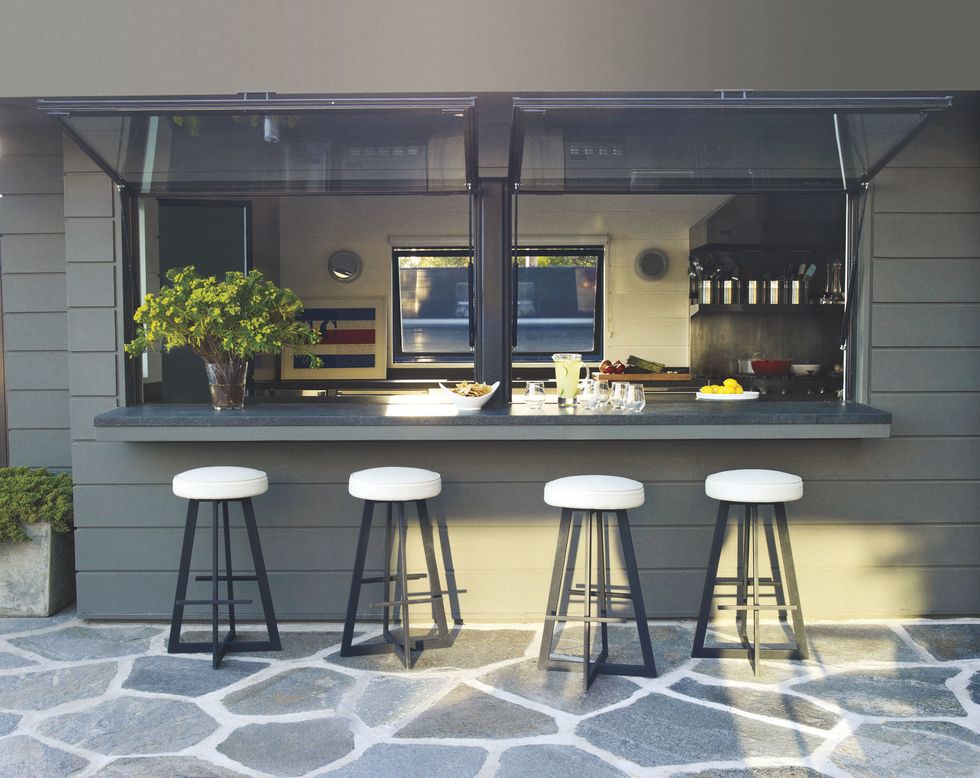 terrace kitchen bar with several white top stools on a stone floor