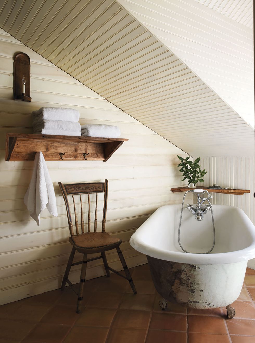 old white standalong tub under an eaved room with tongue and groove paneling and a simple wood shelf and chair