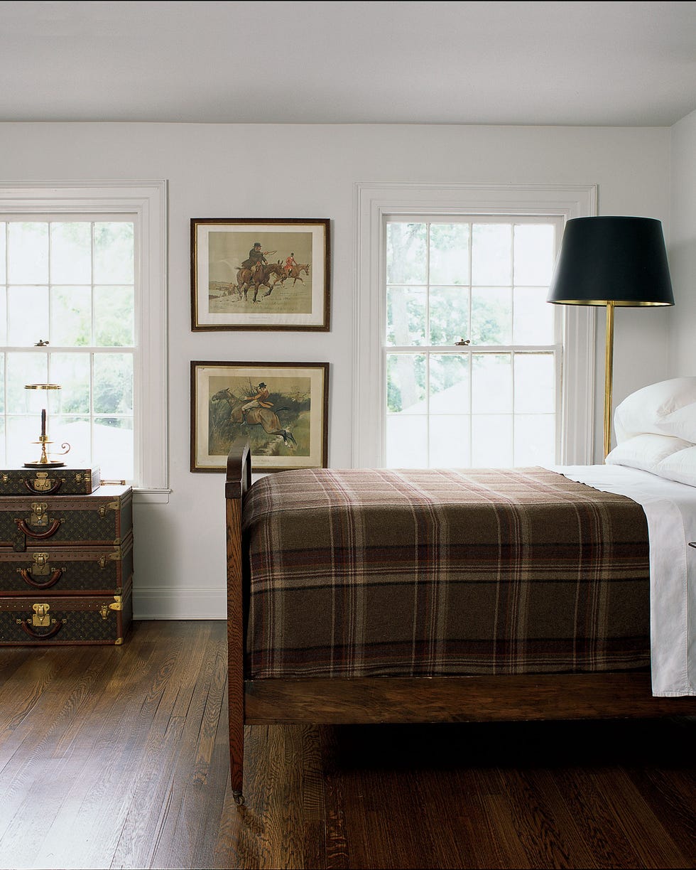 Badgley Mischka - ELLE DECOR bedroom with simple bed with brown plaid cover and prints on the wall and and gold lamps with black shades