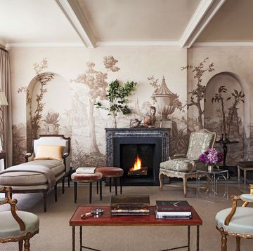 classical living room with chaises and armchairs and a back wall a landscape wall covering with trees and urns and a black fireplace set into the wall