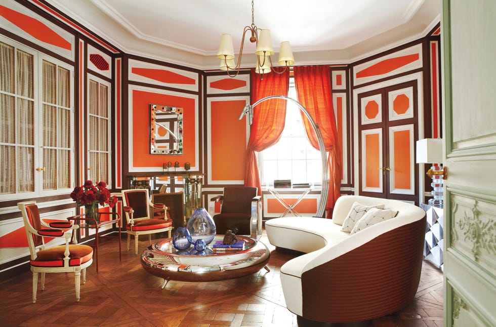 a large oval living room with orange walls and white plaster with a large round golden table and a large rounded white sofa on parquet floor