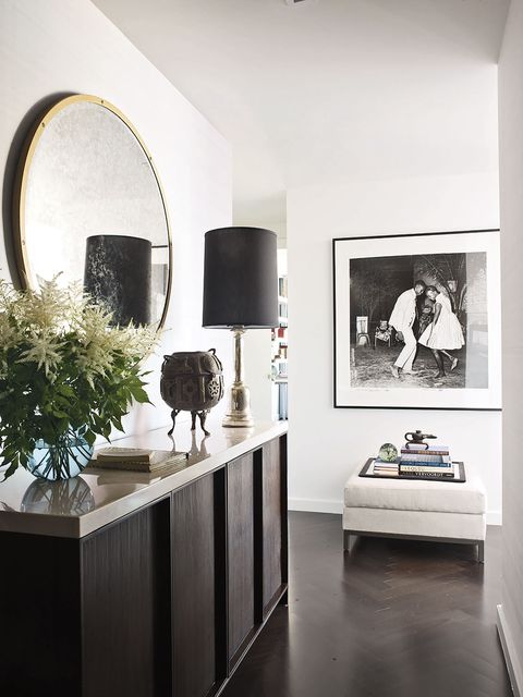 in the entry a console by calvin klein home holds a vintage lamp and a brass vessel, the mirror is by restoration hardware, and the photograph is by malick sidibé