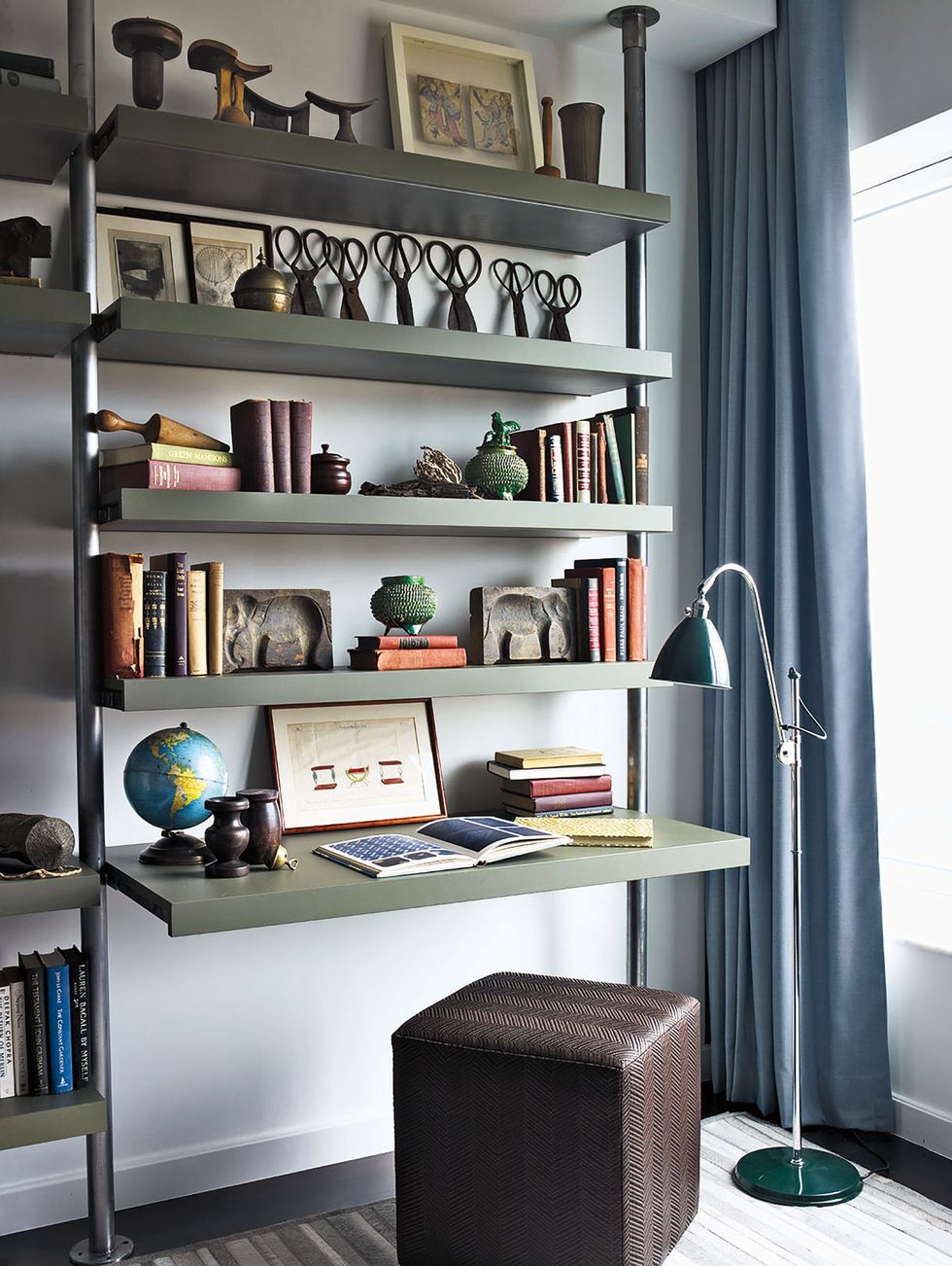 a floor lamp from design within reach stands next to custom made metal and wood shelving  the ottoman is by calvin klein home
