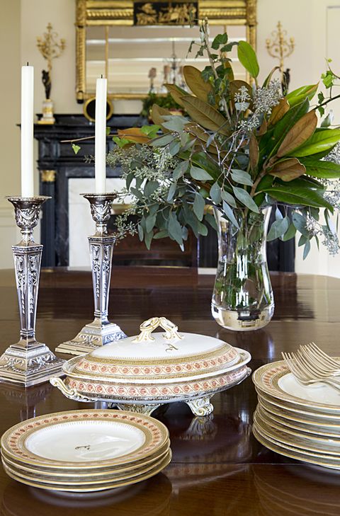 a table with a stack of plates and a vase and candlesticks