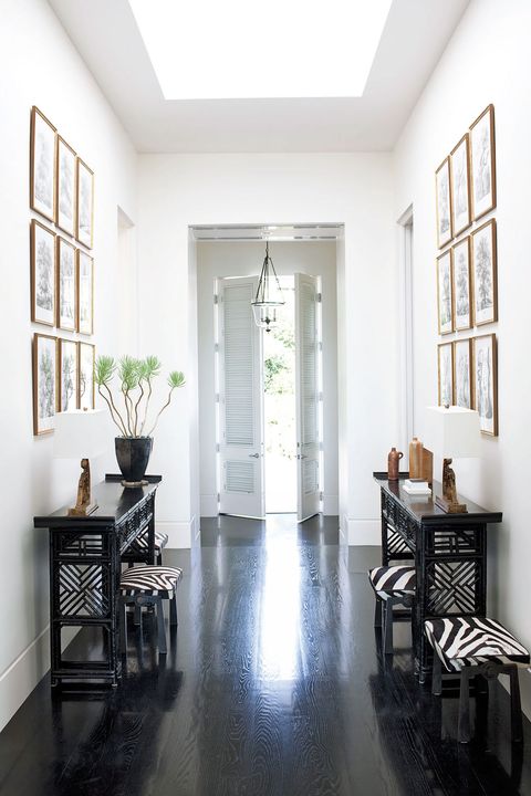 long entry way with dark floors and white walls and flanked by slim black asian style consoles with zebra prints on the framed patterned stools above and slatted doors at the end