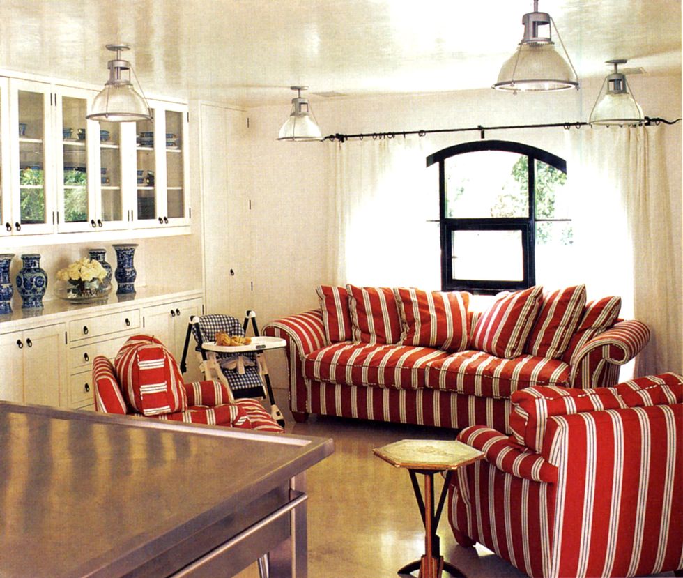 a kitchen  family seating area room framed with cushy striped red sofas a small gold side table and a baby's high chair in a blue check fabric on the seat