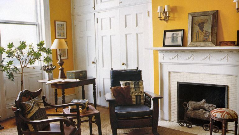 yellow painted library room with a white painted fireplace and some mismatched chairs and small tables and behind them panel inset white painted doors