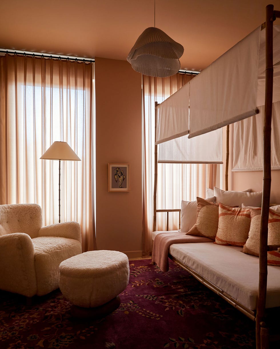 Guest Bedrooms - ELLE DECOR a day bed in blush tones with lots of pillows with darker constrasting ribbons and light shades on the sides with a deep fuzzy chair with ottoman across it and similar toned sheer draperies on the two tall windows