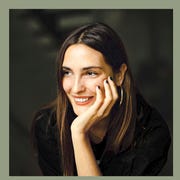 Pia Riverola - Elle Decor Winter 2022 pia riverola portrait, hand leaning on cheek, smiling and a bottle with box of rowse beauty oil
