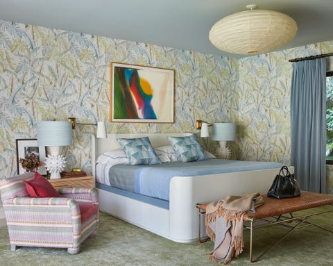 bedroom with white platform bed with blue sheets and pillows a greenish marbled carpet and a pink striped chair next to it