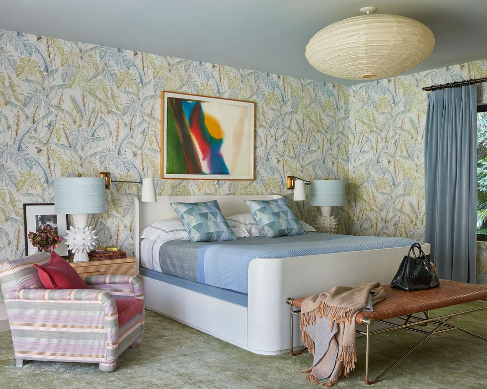bedroom with white platform bed with blue sheets and pillows a greenish marbled carpet and a pink striped chair next to it