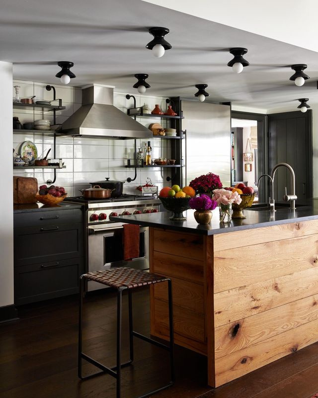 kitchen with open shelving and raw wood island with mesh black stools and a professional viking stove black x shaped lights with white globes hang from the ceiling