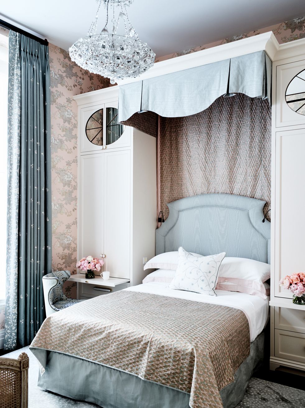 small bed with blue upholstered headboard and canopy tucked in between two tall white closets on either side with doors and round mirrors and trays that slide out at bed level to act as a nightstand