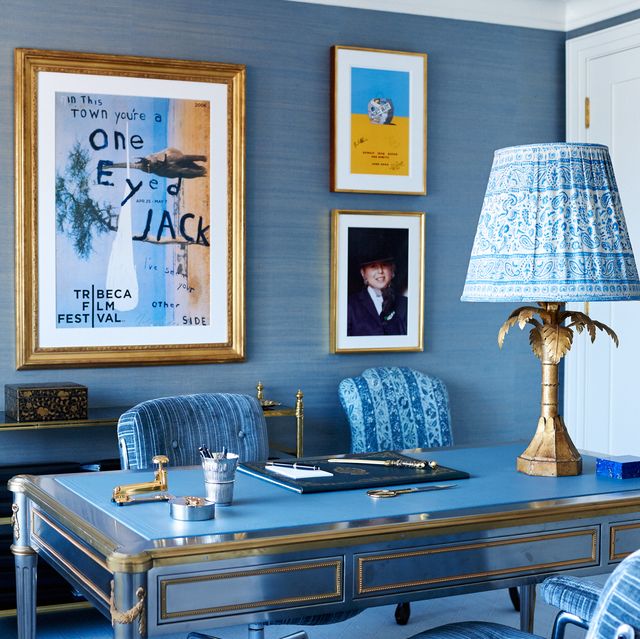 office with blue wall covering, blue upholstered chairs and blue lampshade and gallery of frames behind