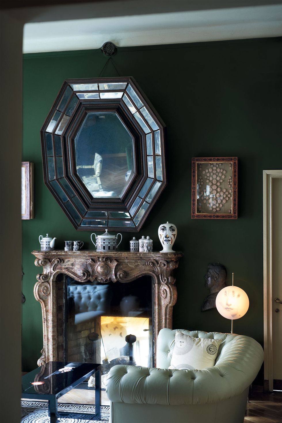 a fireplace in a room with tufted leather sofa and art deco mirror over the mantel filled with objects