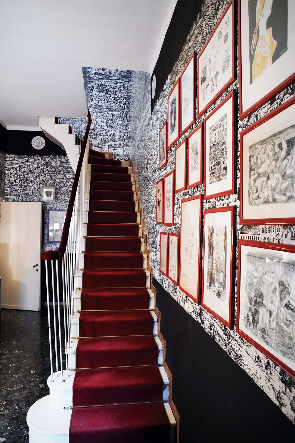 a red carpeted staircase with paintings on the walls covered in a back and white toile like wall covering