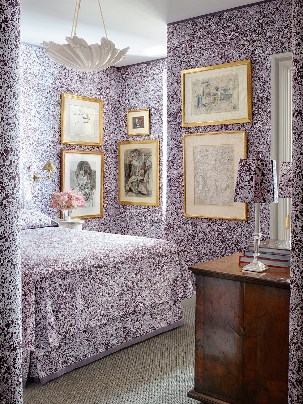 Room, Interior design, Furniture, Wall, Property, Wallpaper, Purple, House, Living room, Bedroom, room with wallpaper bedding and lampshade in the same purple color and splatter print with art hanging on the walls